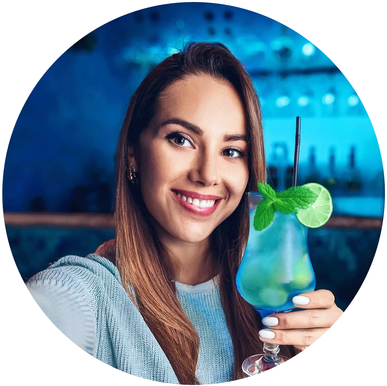 Eine lächelnde Frau hält in einer Bar einen blauen Cocktail mit Minze.