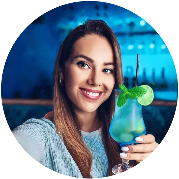 Eine lächelnde Frau hält in einer Bar einen blauen Cocktail mit Minze.