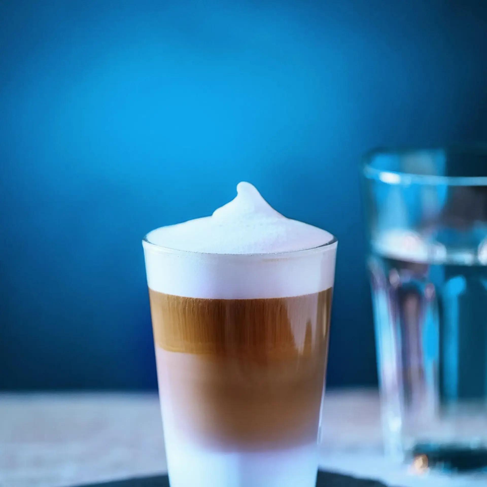Ein Glas mit geschichtetem Kaffeegetränk steht neben einem Wasserbecher.