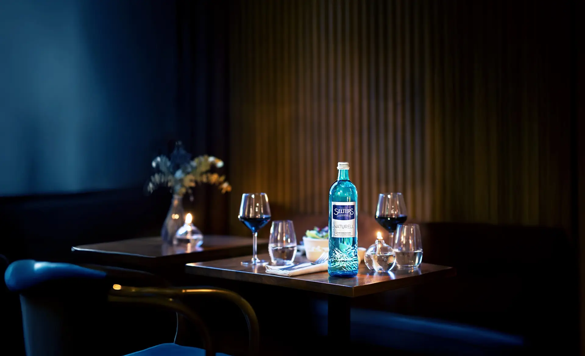 Ein gut beleuchteter Tisch in einem dunklen Raum mit einer Flasche Wasser und zwei Gläsern.