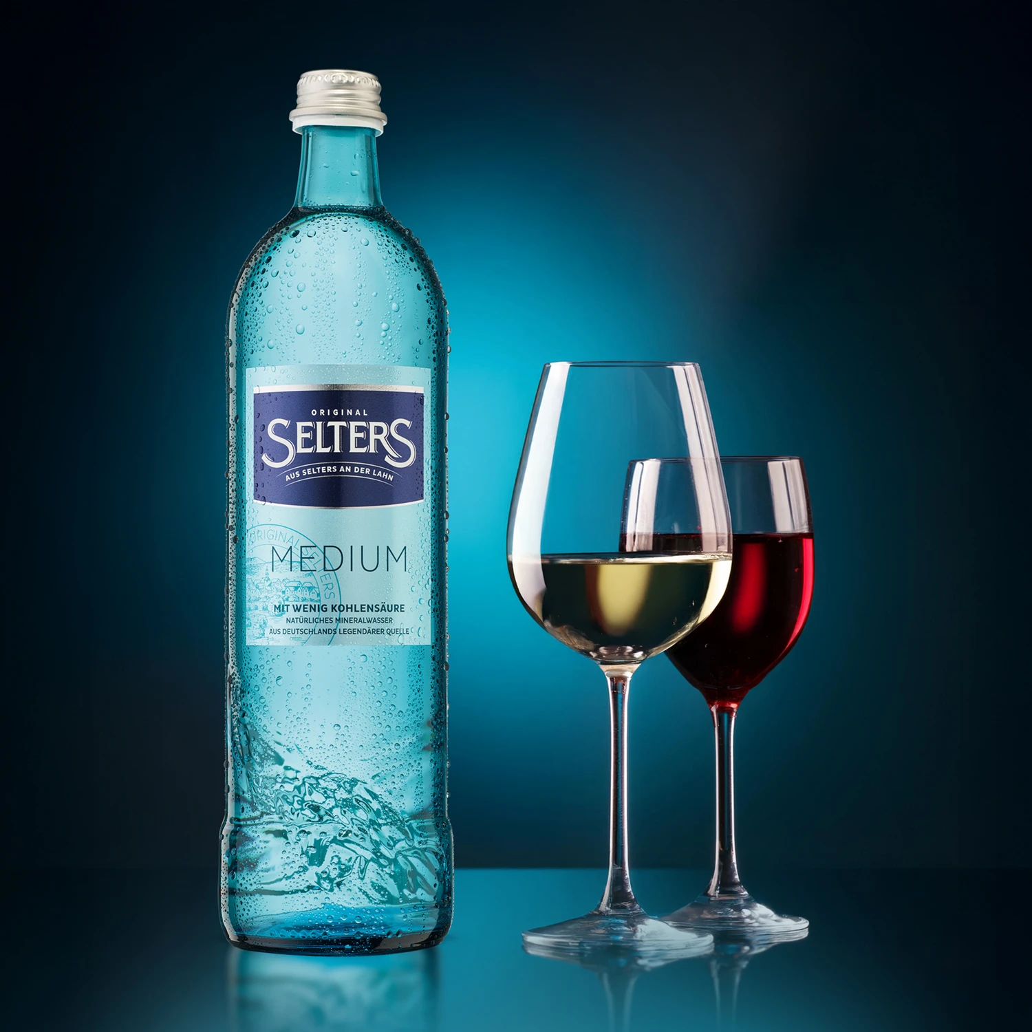 Eine klare Glasflasche mit Wasser und zwei Weingläser, eines mit rotem und eines mit weißem Wein, stehen auf einer Oberfläche.