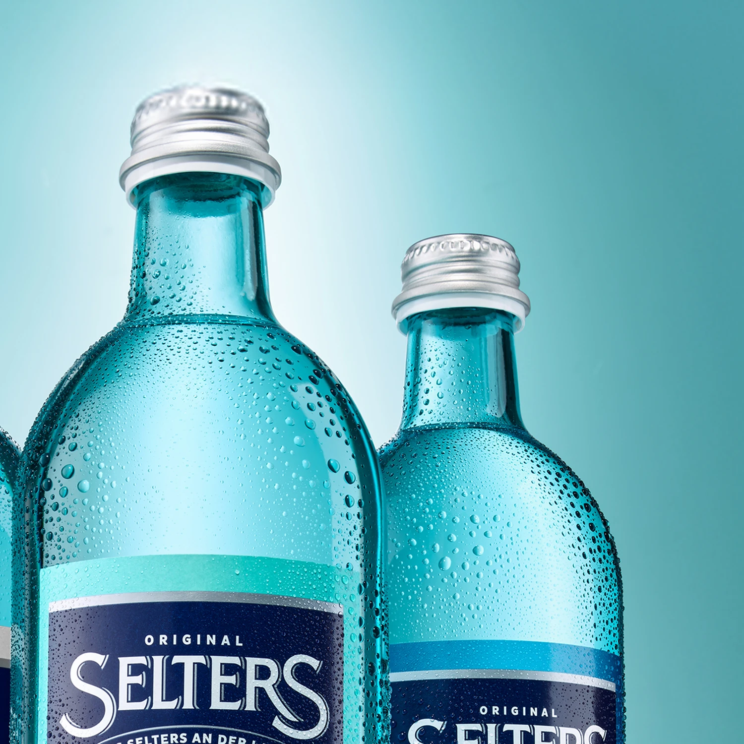 Zwei blaue Glasflaschen mit Wassertröpfchen stehen vor einem türkisfarbenen Hintergrund.