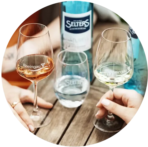 Zwei Personen stoßen mit Weingläsern an einem Holztisch an.