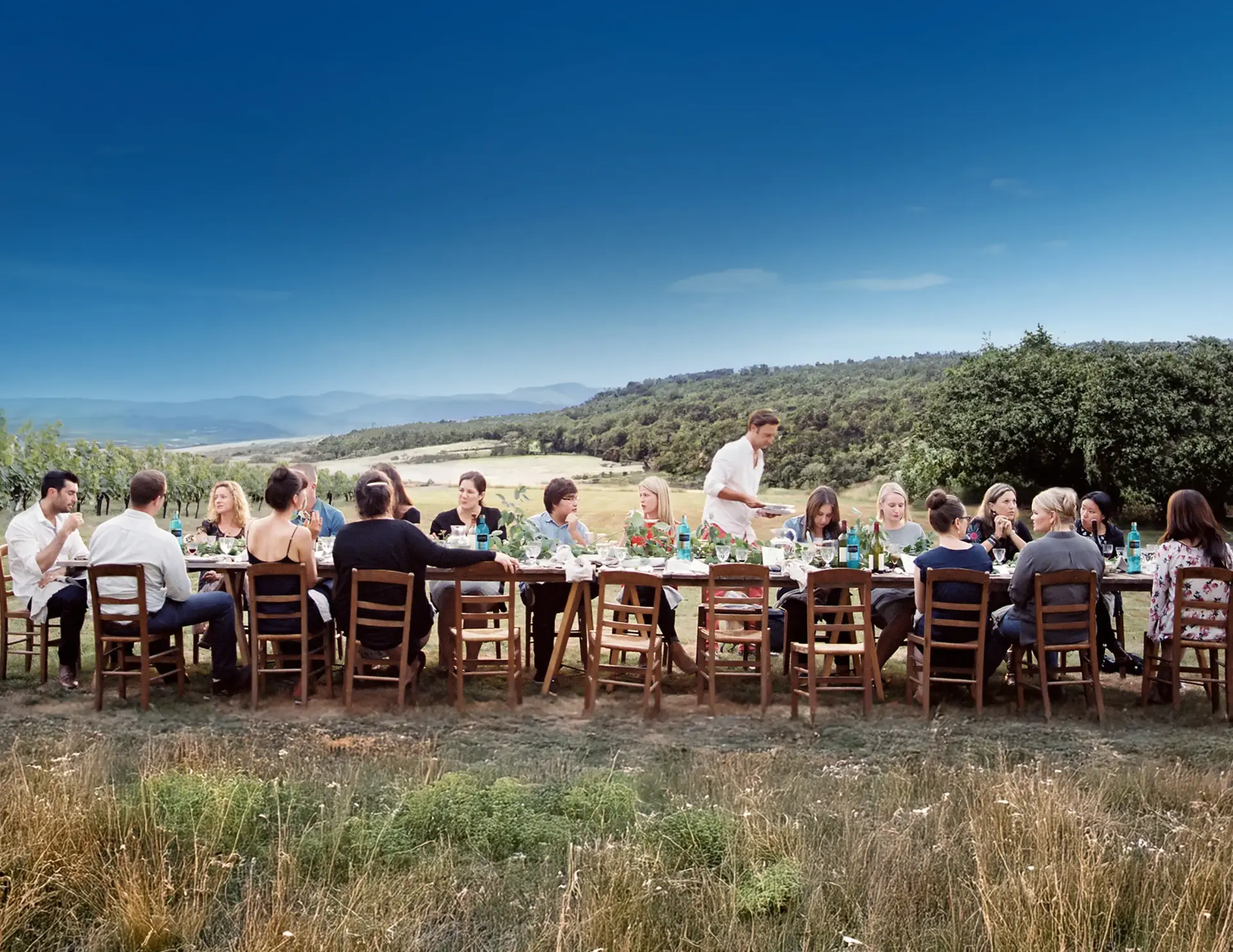 Eine Gruppe von Menschen isst gemeinsam an einer langen Tafel im Freien.