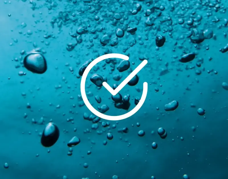 Eine blaue wässrige Oberfläche ist bedeckt mit vielen kleinen Blasen; eine weiße Haken-Ikone befindet sich mittig.