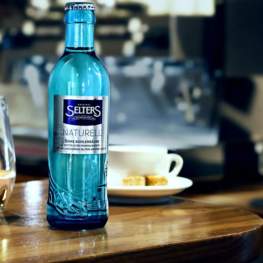 Eine blaue Wasserflasche steht auf einem Holztisch neben einer Tasse.