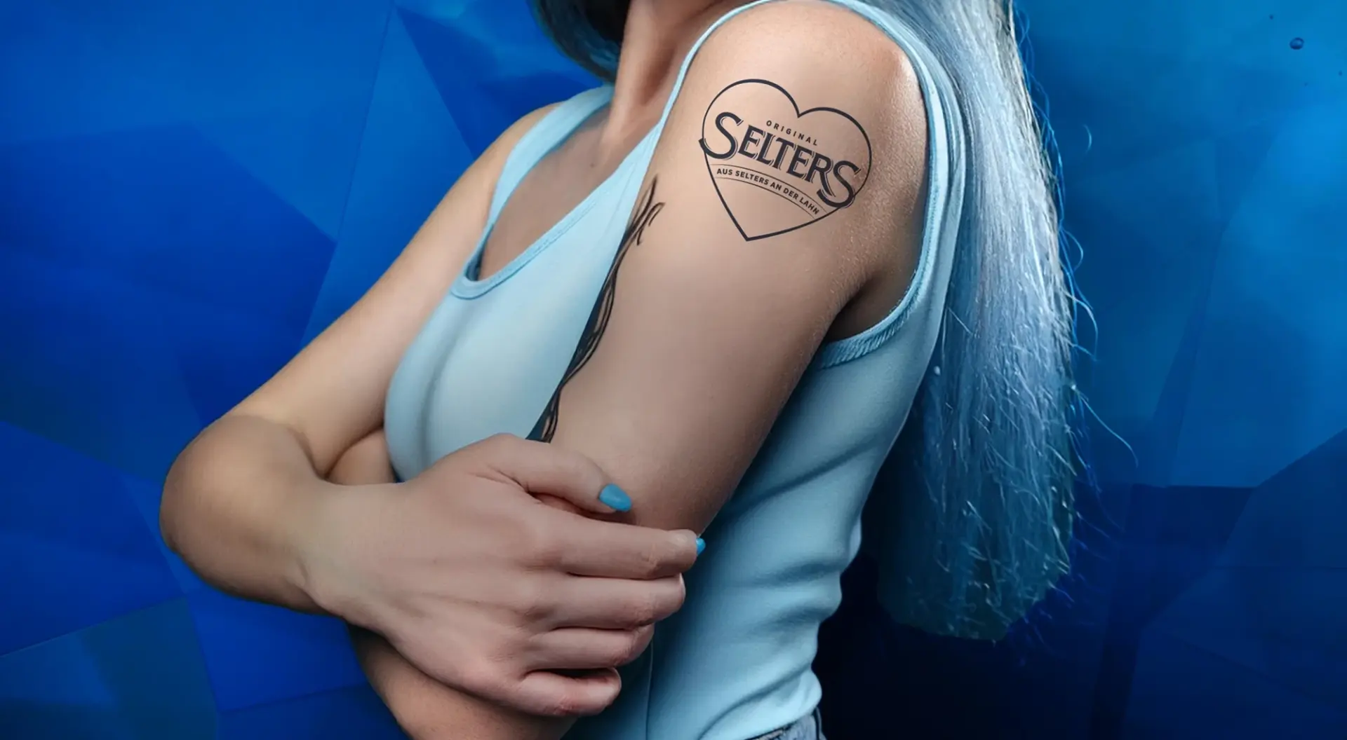 Eine Person mit blauem Haar zeigt eine Tätowierung am Oberarm.